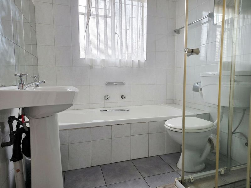 A dated bathroom featuring a pedestal basin, built-in bathtub, toilet, and a glass shower enclosure with tiled finishes throughout.