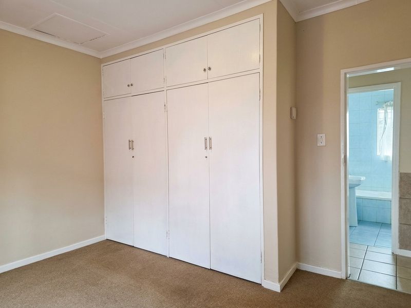 A clean, empty bedroom featuring built-in cupboards with overhead storage and carpeted flooring, with an adjacent view into a tiled bathroom.