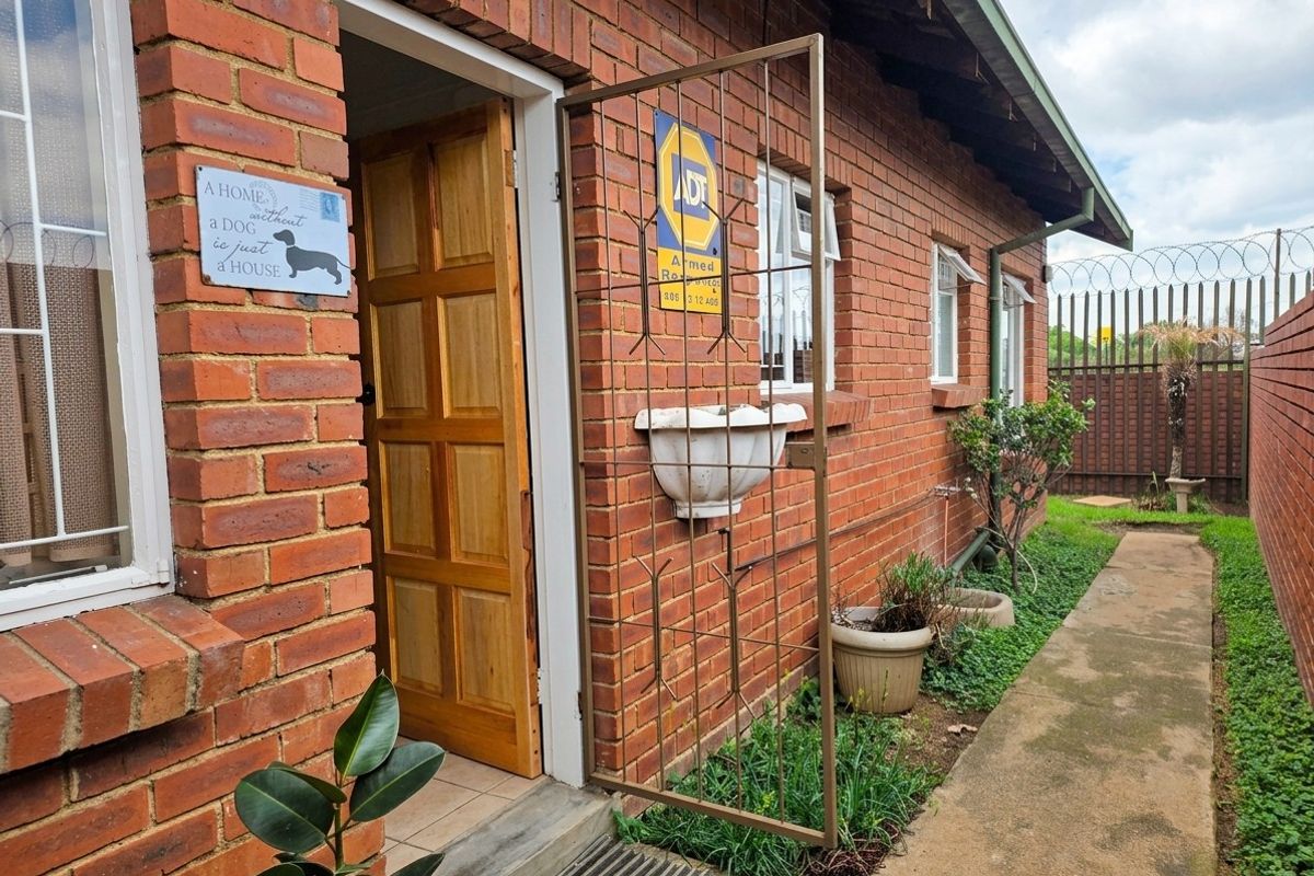 Rear exterior view of a face brick townhouse featuring a security gate, timber entrance door, and a concrete pathway leading along the side.