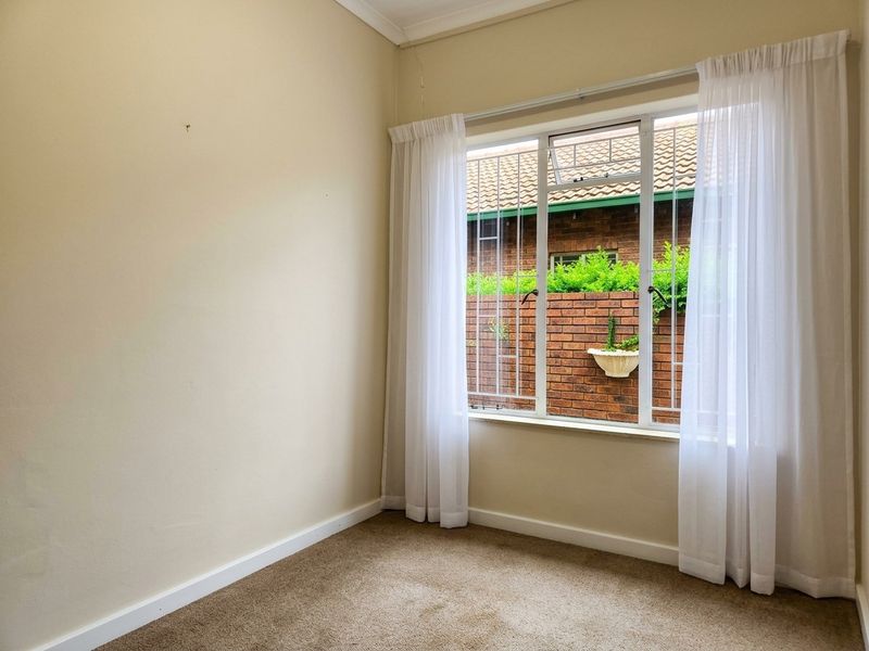 An empty bedroom featuring carpet flooring, neutral walls, and a window fitted with security bars.