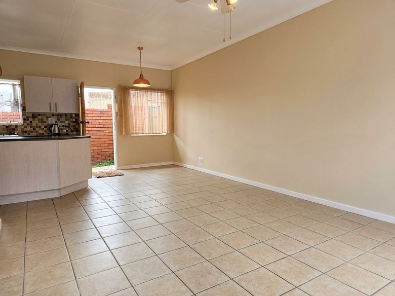 Open plan living area featuring tiled flooring, a compact kitchen with mosaic backsplash, and direct access to an outdoor area.