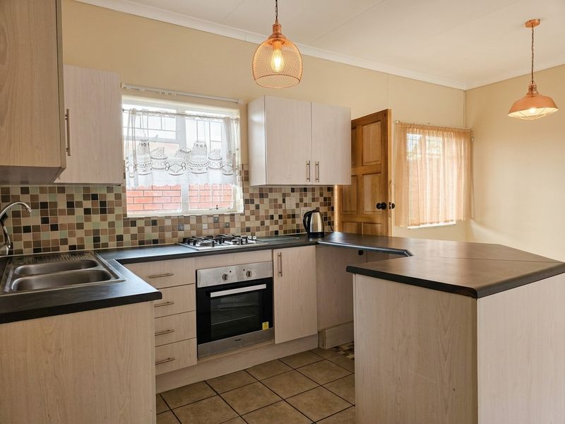 A functional kitchen featuring light wood-finish cabinetry, dark laminate countertops, a mosaic tile backsplash, and built-in oven with gas hob.