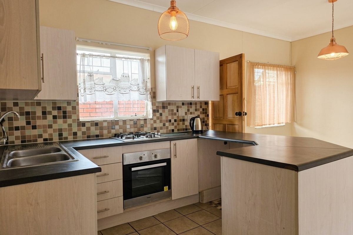 A functional kitchen featuring light wood-finish cabinetry, dark laminate countertops, a mosaic tile backsplash, and built-in oven with gas hob.
