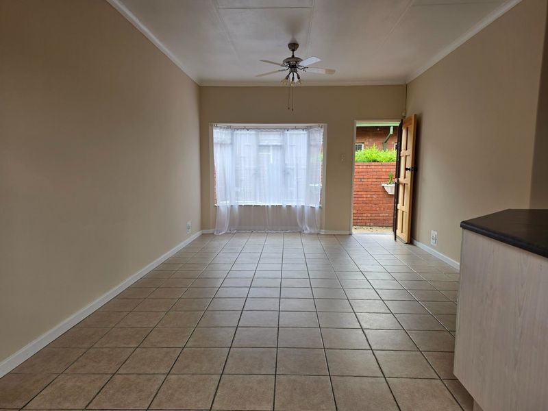 An empty living area featuring ceramic floor tiles, a ceiling fan, and a bay window with direct access to the exterior.