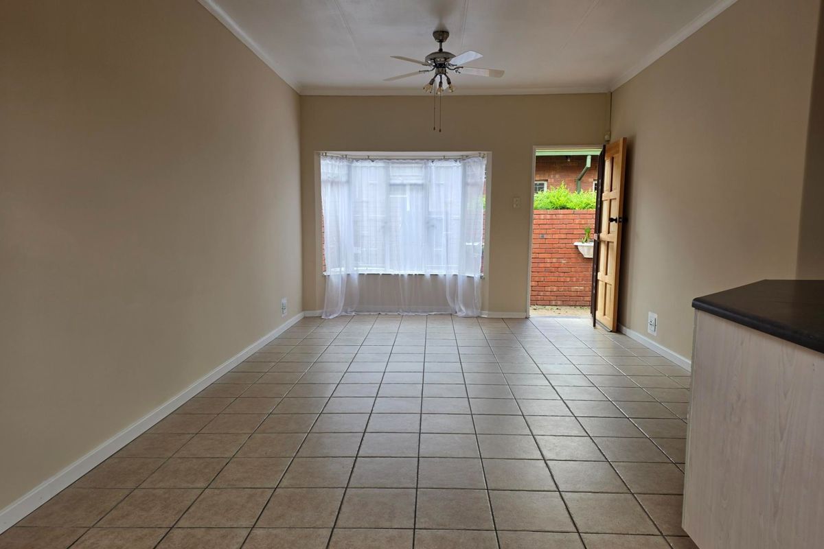 An empty living area featuring ceramic floor tiles, a ceiling fan, and a bay window with direct access to the exterior.