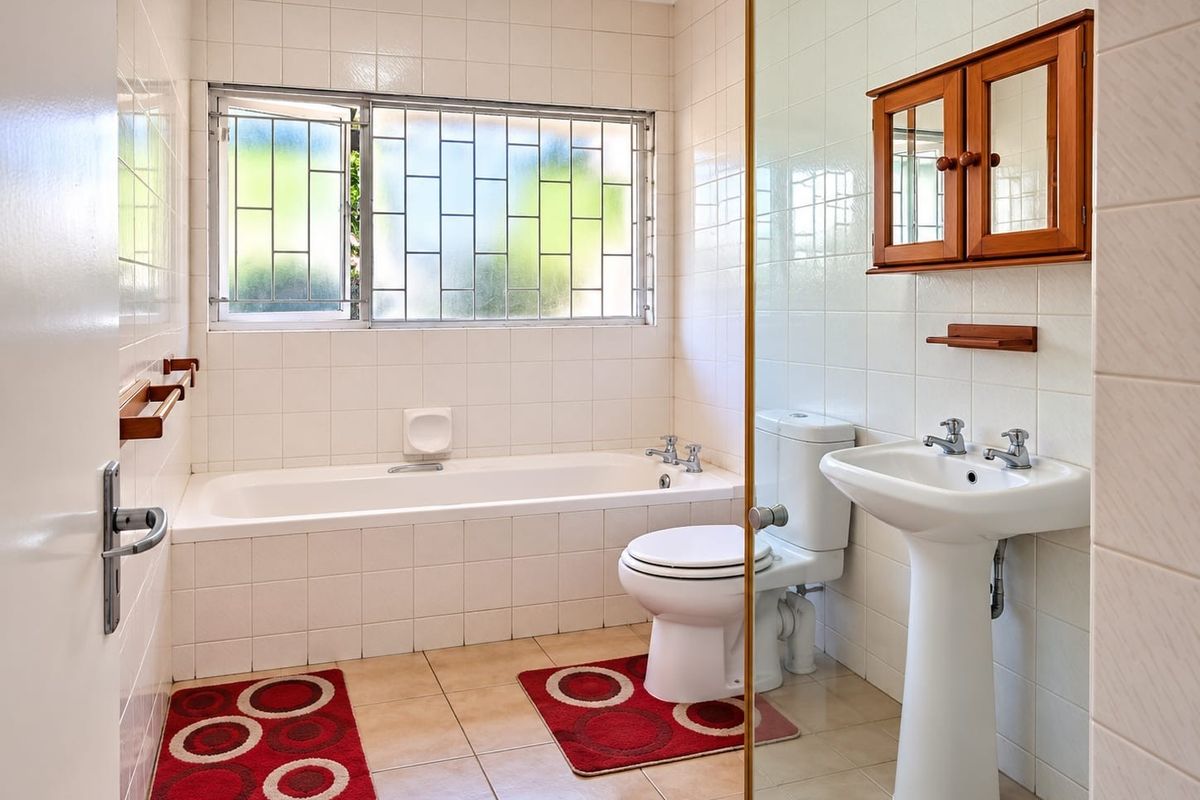 A functional bathroom featuring a built-in bathtub, pedestal basin, toilet, and wall-mounted medicine cabinet, finished with neutral wall and floor tiles.