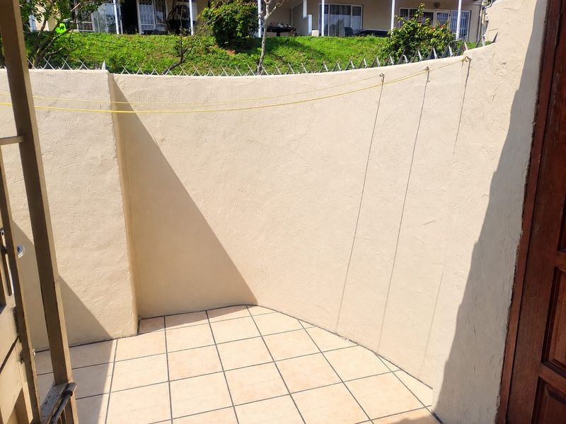 A private outdoor utility area featuring tiled flooring, a perimeter wall with security spikes, and a fixed washing line.
