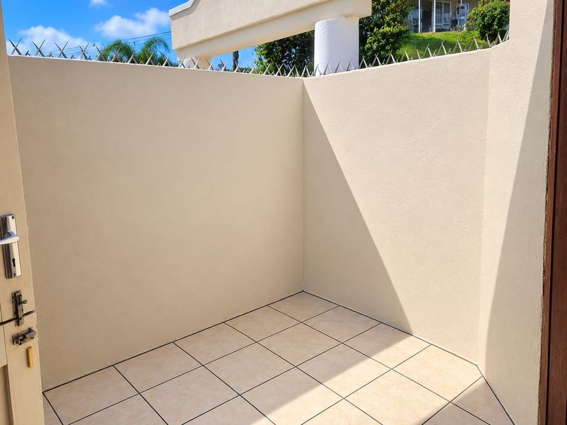 A private, tiled outdoor patio area enclosed by high plastered boundary walls featuring security spikes for added safety.