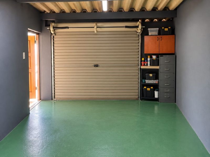 A well-maintained garage featuring a roller shutter door, smooth painted green flooring, and integrated storage cabinetry.
