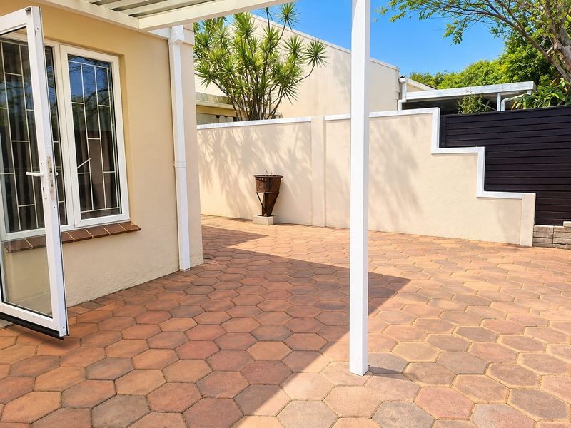A well-maintained paved patio area featuring a pergola, secure boundary walls, and direct access to the interior through double glass doors.