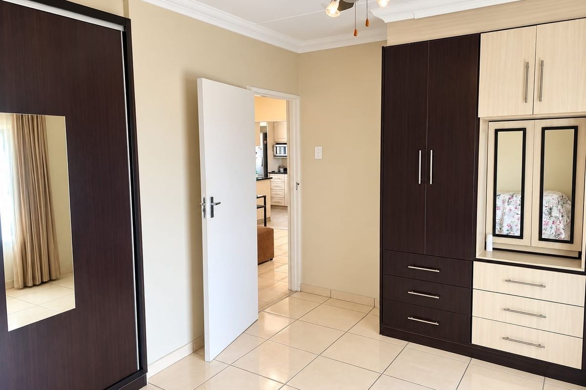A well-maintained bedroom featuring extensive built-in cabinetry, tiled flooring, and a ceiling fan, with a view through to the adjacent kitchen area.