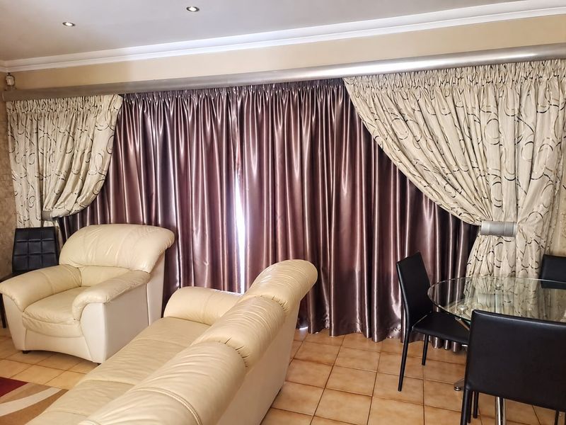 A living area featuring tiled flooring and recessed downlights, with large curtains covering the window or sliding door area.