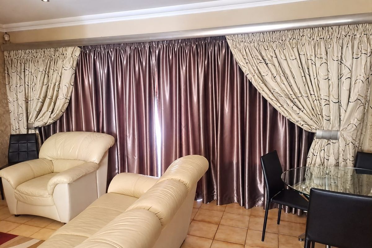 A living area featuring tiled flooring and recessed downlights, with large curtains covering the window or sliding door area.