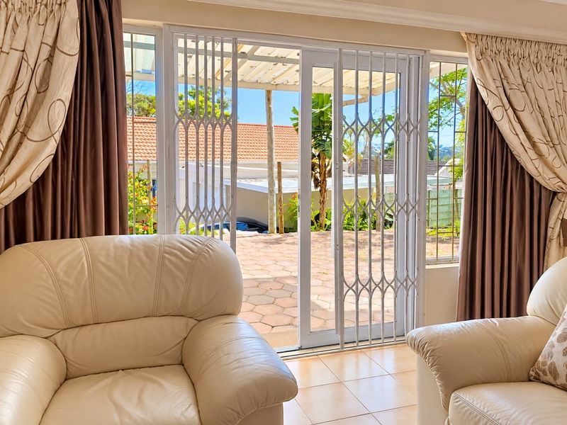 A bright living room featuring tiled flooring and a sliding glass door with a security gate, providing direct access to an outdoor patio area.