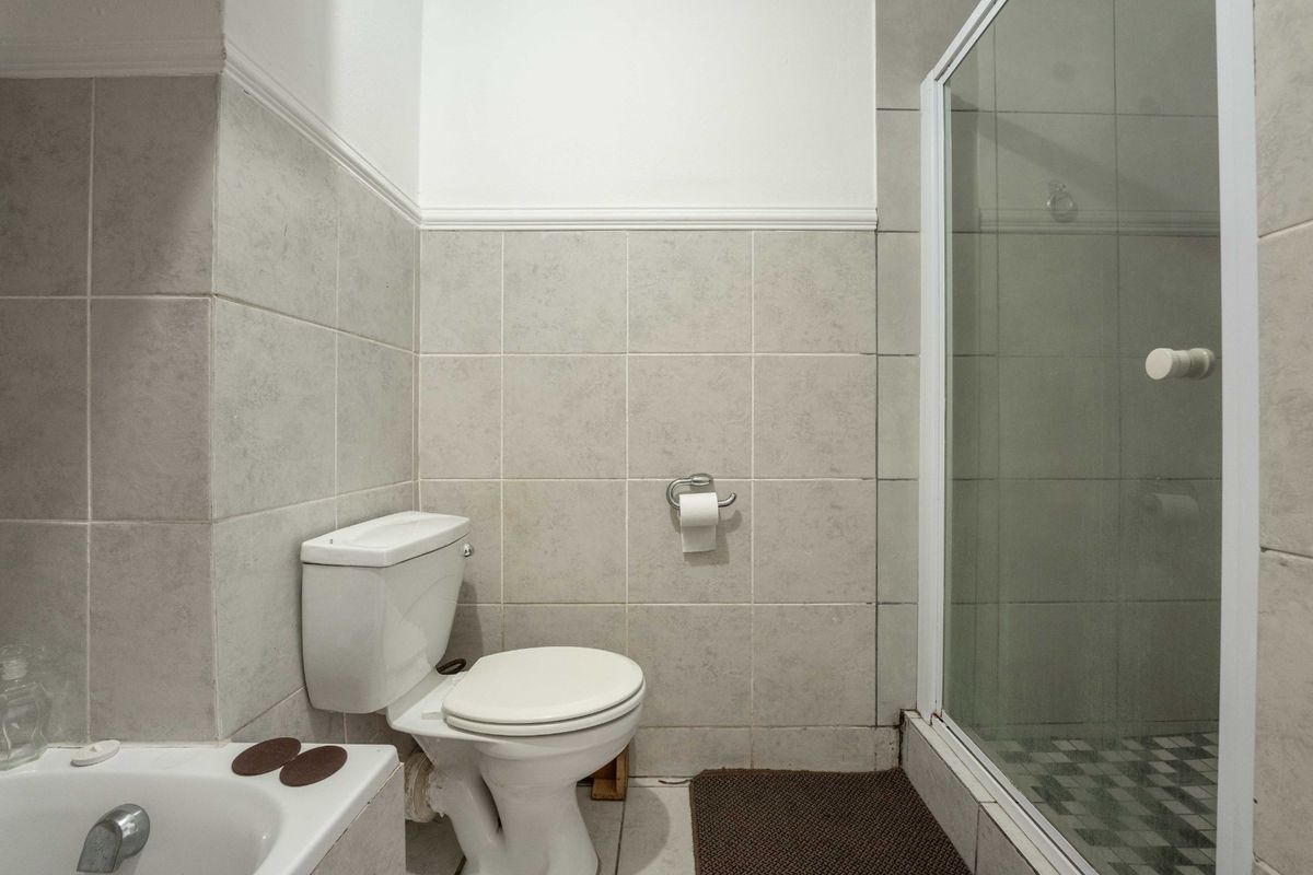 A functional bathroom featuring a bathtub, a separate shower enclosure, and a standard toilet with neutral ceramic wall and floor tiling.
