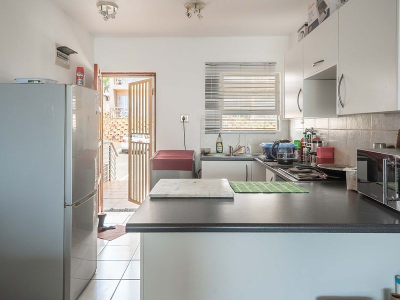 Functional kitchen featuring built-in cabinetry, laminate countertops, a stainless steel sink, and a hob, with direct access to an exterior entrance.