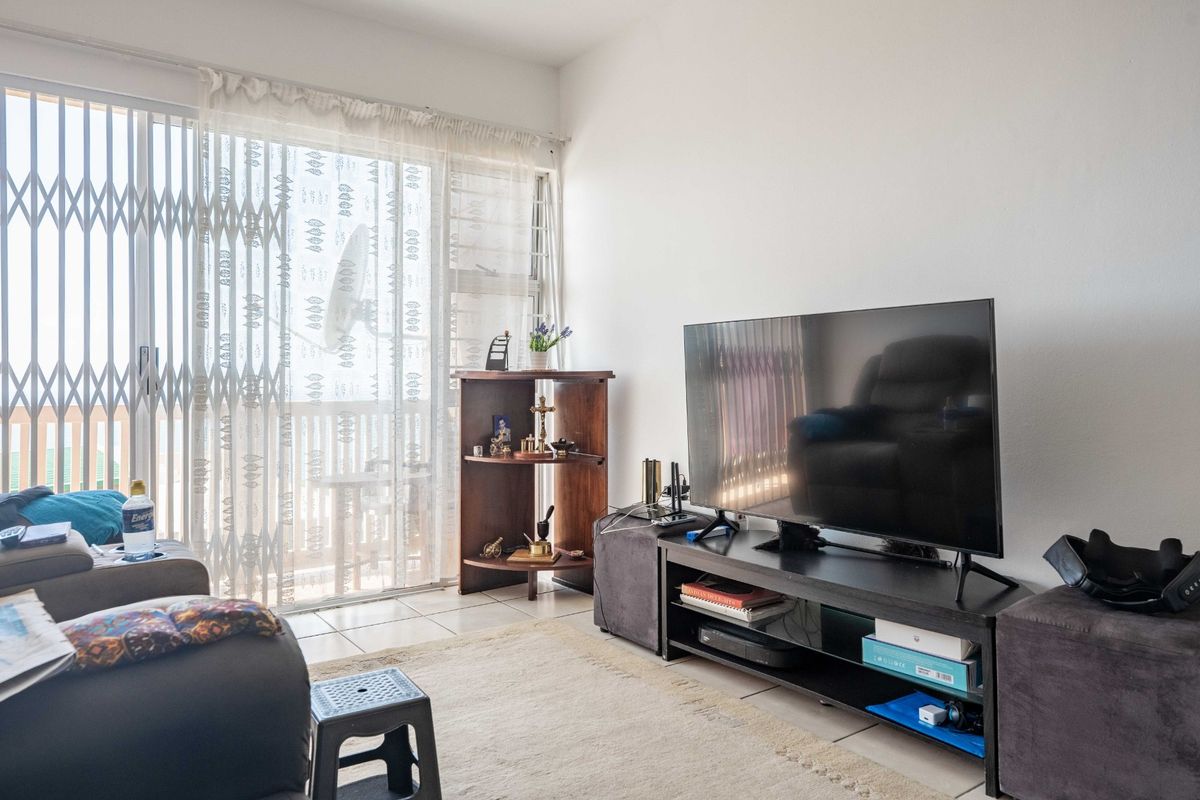 A living room featuring tiled flooring and a sliding glass door with a security gate, providing access to an outdoor area.