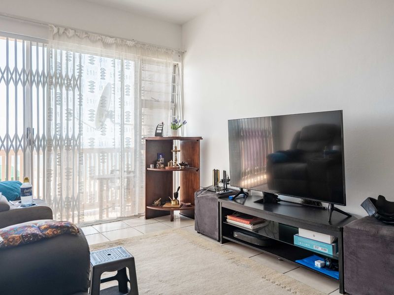 A living room featuring tiled flooring and a sliding glass door with a security gate, providing access to an outdoor area.