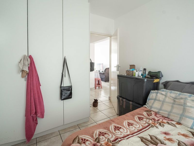 A bedroom featuring built-in wardrobes and tiled flooring, with a doorway leading to an adjacent living area.