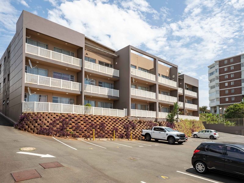 A multi-story apartment complex featuring private balconies, secure parking bays, and a landscaped retaining wall at the front entrance.