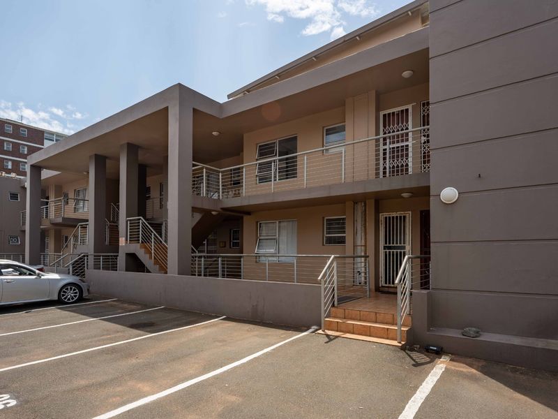 Exterior view of a multi-story apartment complex featuring paved parking, concrete staircases, and secure metal balustrades leading to individual unit entrances.