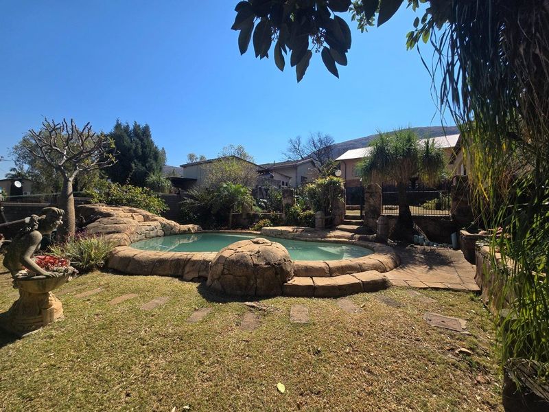 A landscaped backyard featuring a rock-style swimming pool, paved patio area, and established garden surroundings.