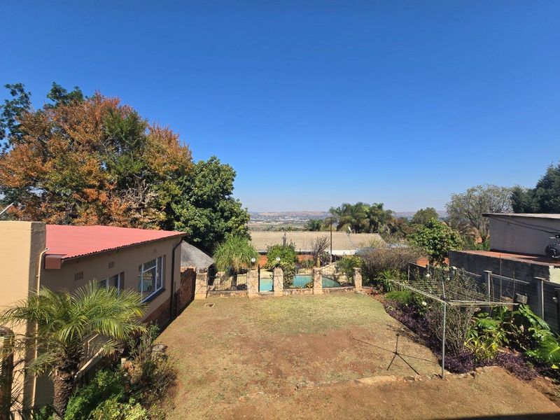 Rear garden view featuring a lawn area, perimeter wall, and a swimming pool in the background with distant landscape views.