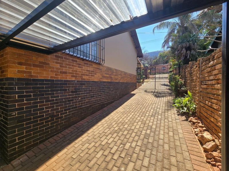 A paved driveway leading to a secure metal gate, featuring a facebrick boundary wall and a covered carport area.