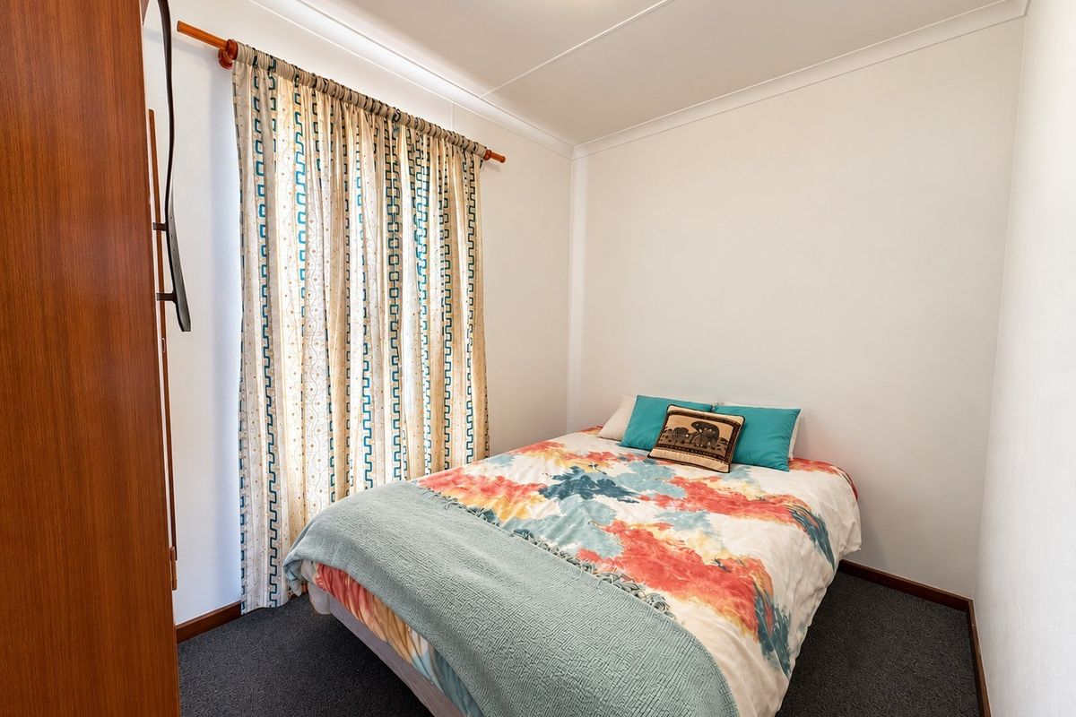 A compact bedroom featuring neutral walls, carpeted flooring, and ceiling cornicing, providing a functional space for rest.