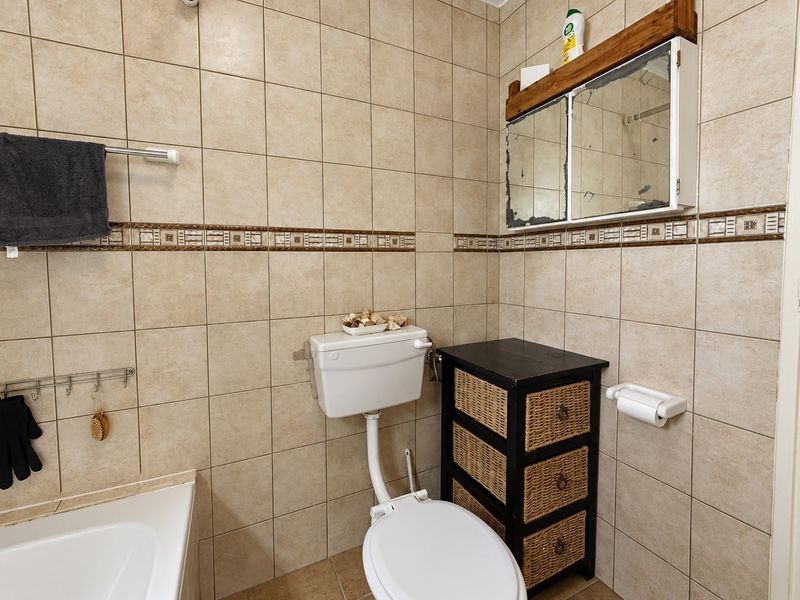 A dated bathroom featuring full-height ceramic wall tiles, a standard toilet, and a bathtub, requiring cosmetic updates to the fixtures and finishes.
