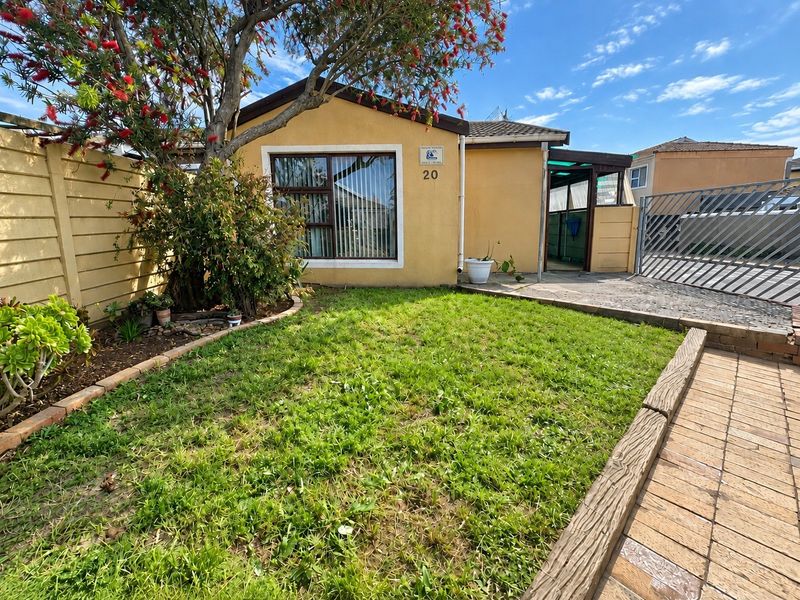 Front view of the property featuring a small lawn, paved driveway, metal security gate, and a covered entrance area.