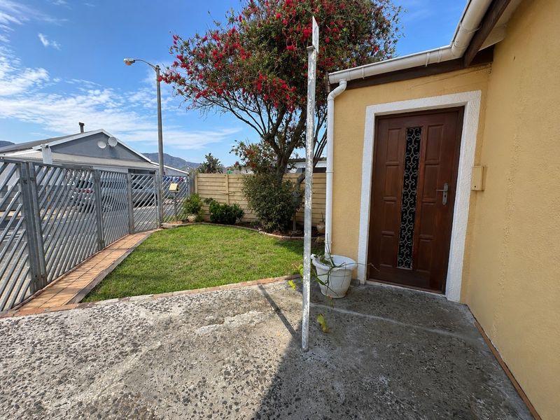 Front entrance area featuring a timber door, concrete patio, and metal security gate, set within a small garden space.