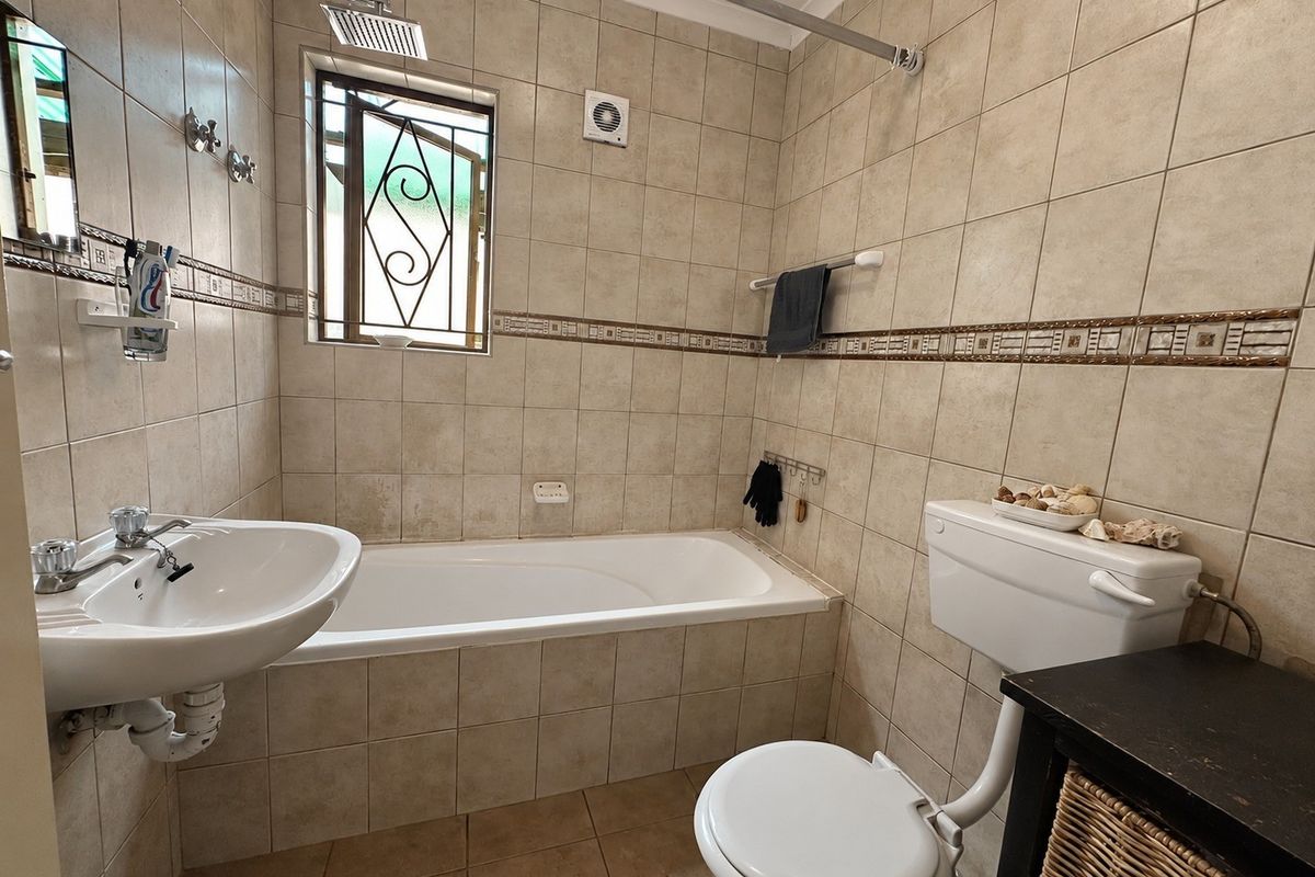 A functional bathroom featuring a bathtub, pedestal basin, and toilet, finished with neutral wall and floor tiling.