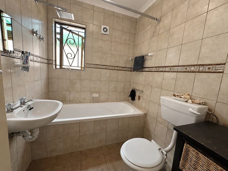 A functional bathroom featuring a bathtub, pedestal basin, and toilet, finished with neutral wall and floor tiling.