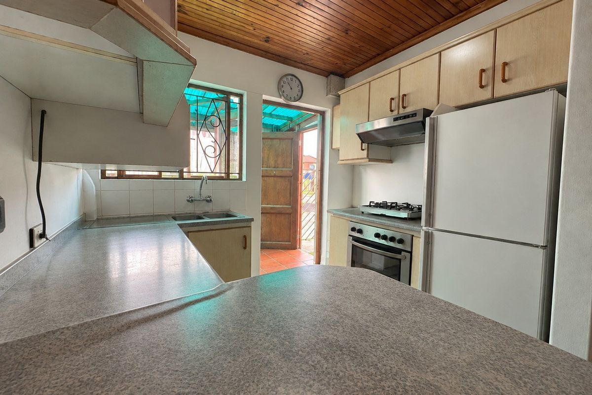 A functional kitchen featuring laminate cabinetry, built-in oven with gas hob, extractor fan, and a timber-paneled ceiling with direct access to an outdoor area.