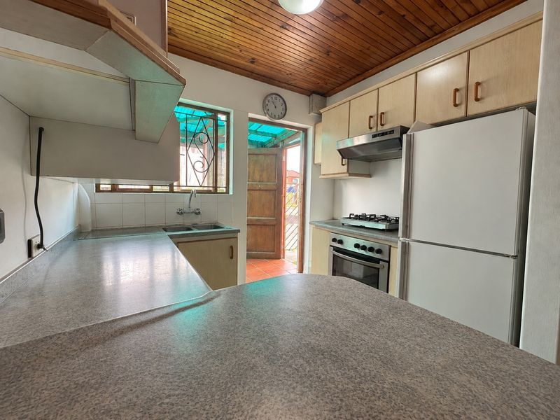 A functional kitchen featuring laminate cabinetry, built-in oven with gas hob, extractor fan, and a timber-paneled ceiling with direct access to an outdoor area.