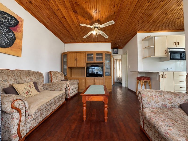 Open-plan living area featuring timber ceilings, laminate flooring, and a functional kitchen with built-in cabinetry and a breakfast bar.