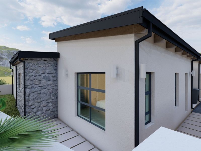 A modern residential exterior featuring stone cladding, black metal window frames, and clean architectural lines set against a scenic landscape.