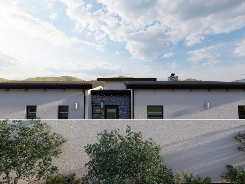 A modern residential facade featuring stone cladding, a sleek metal roof, and a clean boundary wall, set against a scenic mountain backdrop.