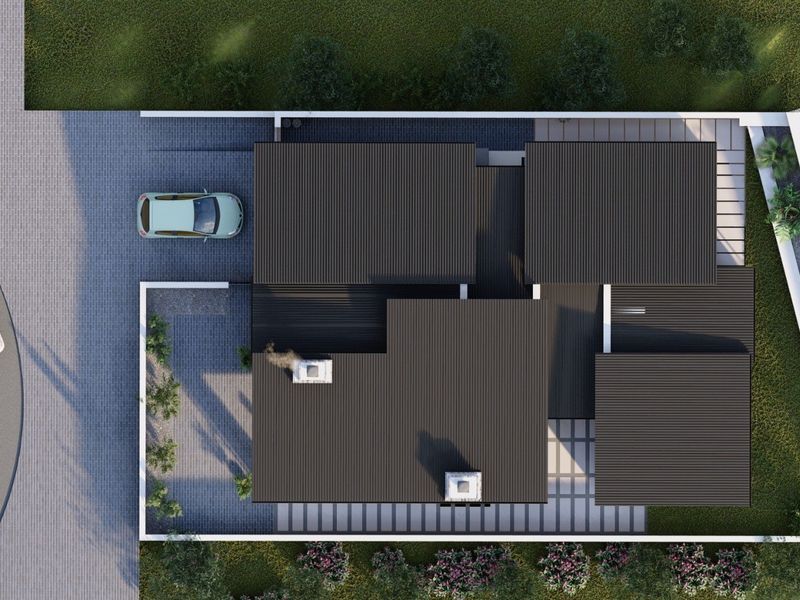 An aerial view of a residential property featuring a modern corrugated metal roof, paved driveway, and perimeter boundary wall.
