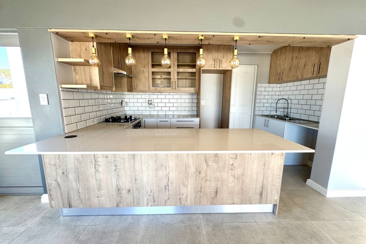 Modern kitchen featuring wood-look cabinetry, quartz countertops, subway tile backsplash, gas hob, and integrated lighting, offering a clean and contemporary aesthetic.