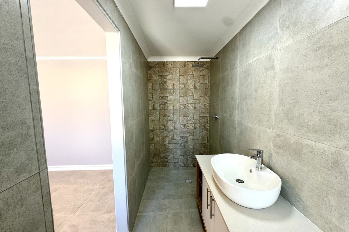 Modern bathroom featuring a vessel sink on a vanity cabinet and a walk-in shower with textured feature tiling.