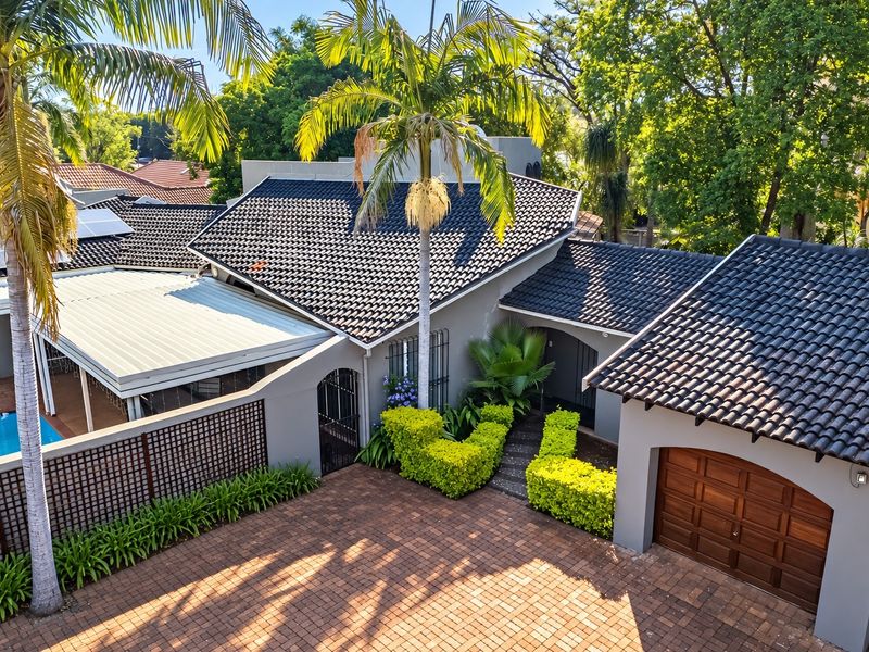 Elevated view of the property entrance featuring a paved driveway, double garage, tiled roof, and a side swimming pool area with a covered patio.