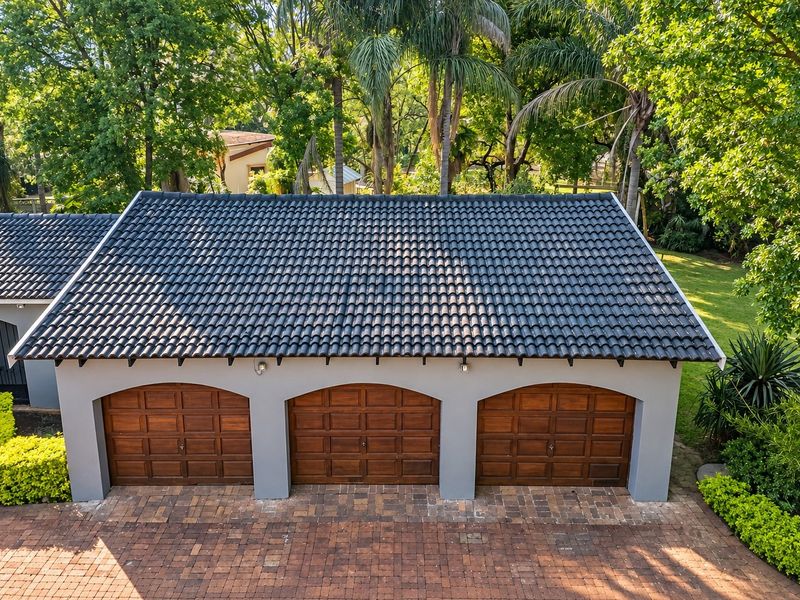 A well-maintained triple garage featuring wooden doors, a dark tiled roof, and a paved driveway set within a lush, landscaped garden environment.