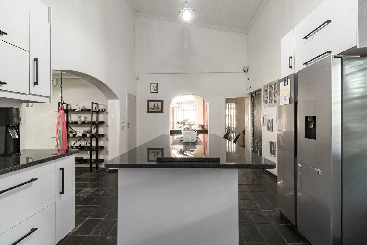 Modern kitchen featuring a central island with granite countertops, white cabinetry, and high vaulted ceilings, finished with dark stone tile flooring.