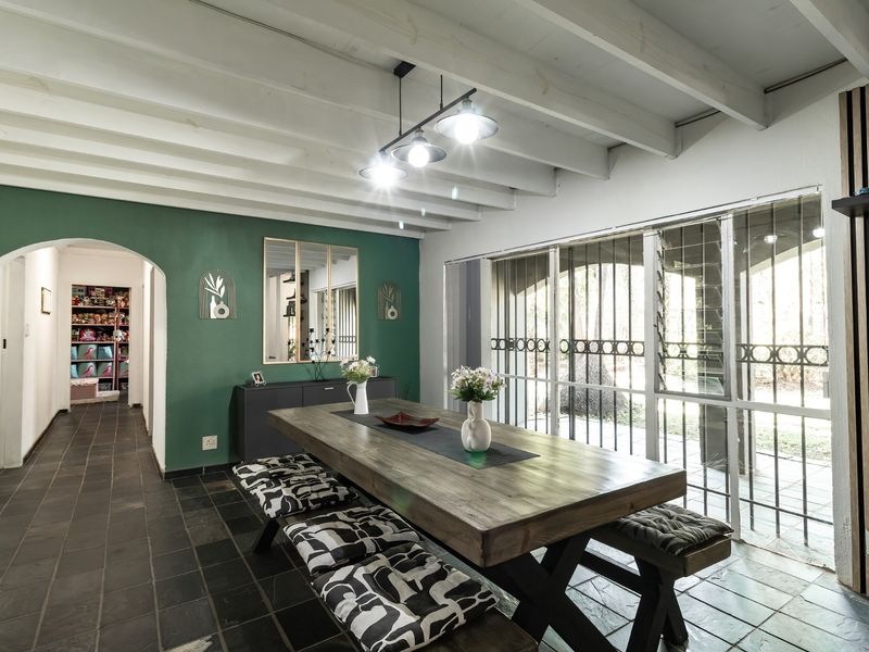 Dining room featuring exposed beam ceilings, slate tile flooring, and an archway leading to a hallway, with large windows and security gates.
