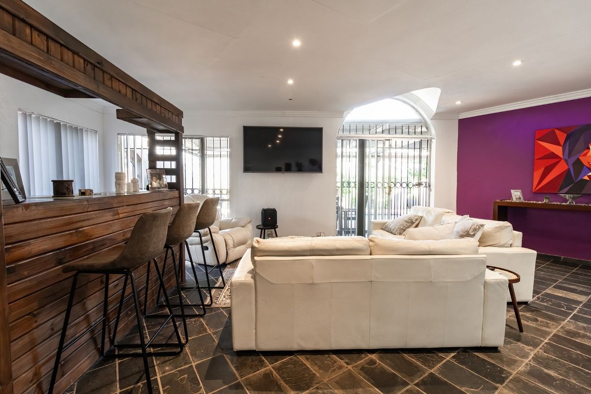 Spacious living area featuring a built-in wooden bar, stone tile flooring, and an arched window with security gate, offering a versatile entertainment space.