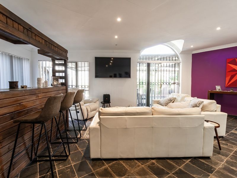 Spacious living area featuring a built-in wooden bar, stone tile flooring, and an arched window with security gate, offering a versatile entertainment space.