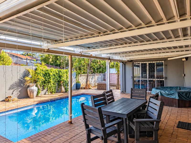 A covered outdoor patio area featuring brick paving, overlooking a private swimming pool with established garden surroundings.