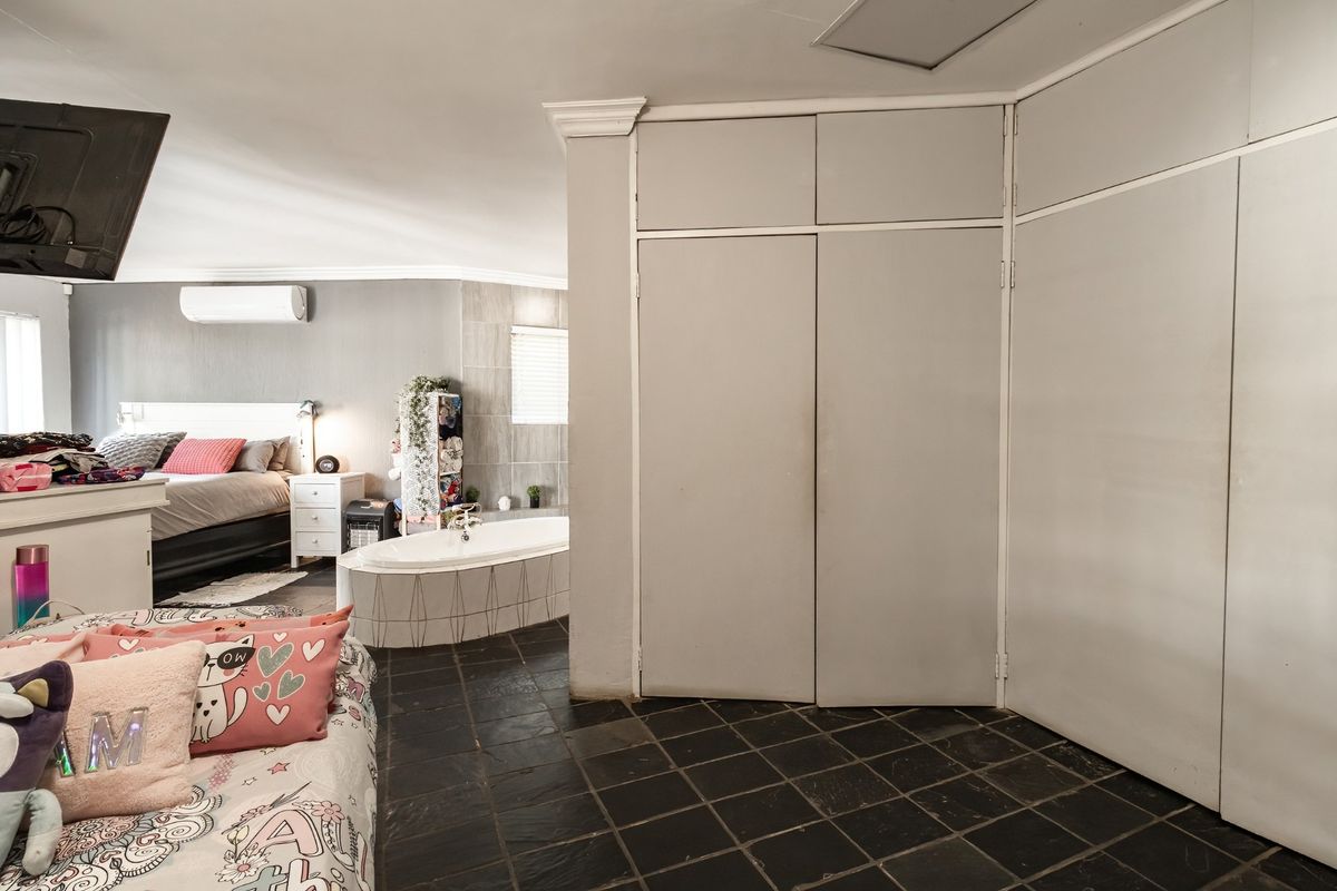 Spacious bedroom featuring built-in cupboards, tiled flooring, a split-system air conditioner, and an integrated bathtub area.